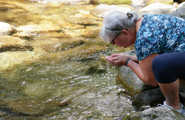 Elderly senior woman holding water from forest river in cup of her hands about to drink it