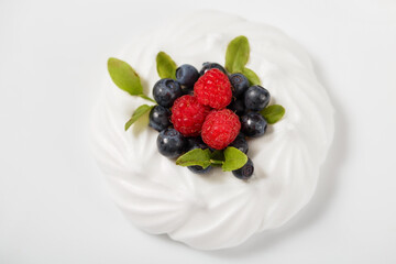 Meringue cake with fresh wild blueberries, raspberries, decorated with fresh leaves. Delicate sweetness close-up on a white background