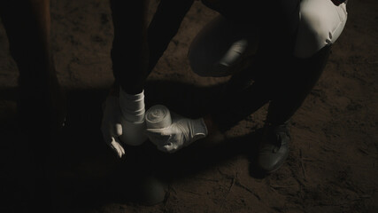 Female horse owner bandaging leg of an injured horse during the nighttime in the horse stable....