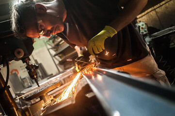 Man working with electric grinder tool on steel structure in factory, sparks flying. Grinding machine in action