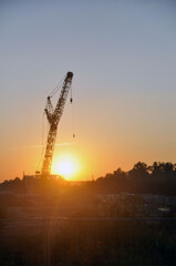 Obraz premium Industrial construction crane against the backdrop of the setting sun.