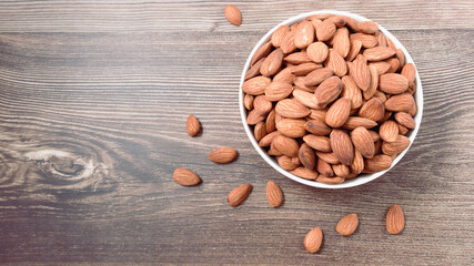 Almond nuts in a white bowl on wooden background, top view, flat lay, top-down, selective focus.copy space.