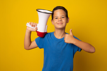 Boy in blue t-shirt holding megaphone with thumb up isolated over yellow background.