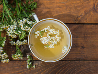 medicinal plant yarrow, a mug with a decoction of yarrow flowers on a wooden background