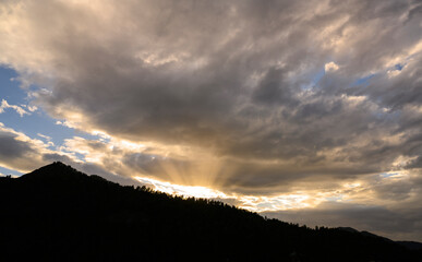 The last ray of the setting sun through the clouds in the mountains