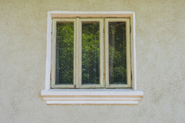 Fototapeta na wymiar Wooden window of the house with white wall. Classic or retro window. The glass reflects the green branches of the trees