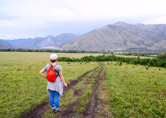 Fototapeta na wymiar A woman on a dirt road leading through a valley to the mountains in the Altai in Russia