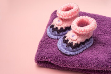 Knitted Baby booties on pink  background and a purple terry towel