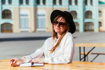 Caucasian girl in a hat and sunglasses smiling while sitting in a cafe in the summer thinks over...