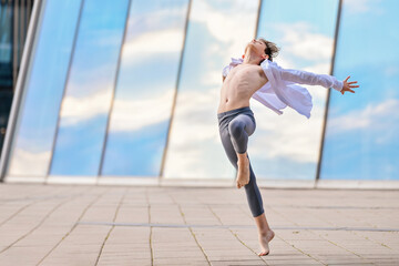 ballet boy teenager expressively dancing against background of sky reflection in glass wall