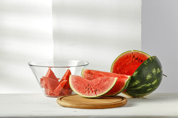 Fresh tasty watermelon on desk and white wall with shadows 