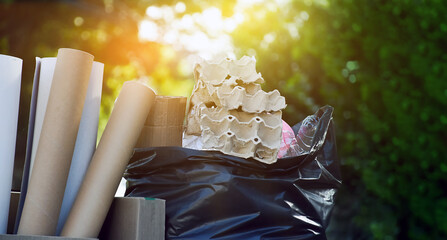 Homeowner is carrying black plastic bag which fulled with garbages, plastic bottles, cartons, milk bottles and used paper to separate and manage garbages at home. Soft and selective focus on garbage.