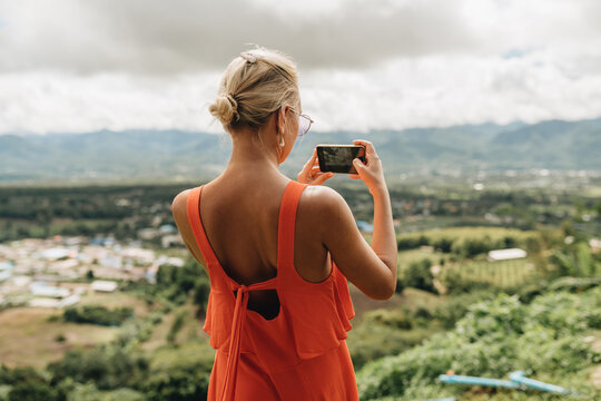 Young woman tourist in orange dress taking picture of amazing view at Yun Lai Viewpoint