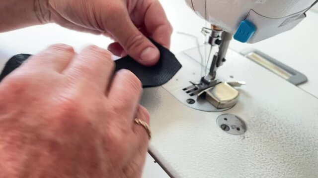 Close up shot of hands of seamstress stitching fabric on sewing machine while working in sewing studio