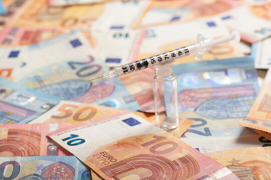 Vial and syringe lying on top of pile of money symbolizing making business thanks to COVID-19 pandemic