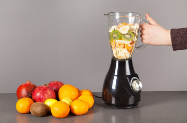 Woman's hand, blender, fruits and gray background.