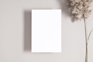 White paper empty blank, dried grass decoration on gray background. White  Invitation card mockup...