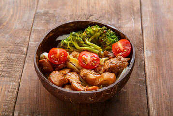 Udon with meat and vegetables in yakiniku sauce in a plate of coconut shells on a wooden table.