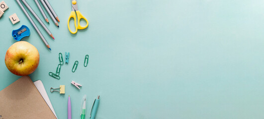Back to school concept. Wooden colored pencils, blank school notebook, paper clips, apple and other stationery on blue background. Pencils for drawing, objects for creativity. Mock up