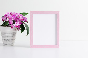 Poster mockup or photo frame with pink orchid flowers on white table.