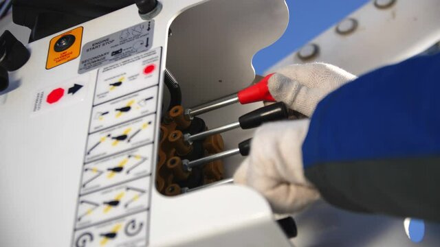 Employee in white gloves controls arm of boom lift truck moving levers on panel on sunny day extreme close view