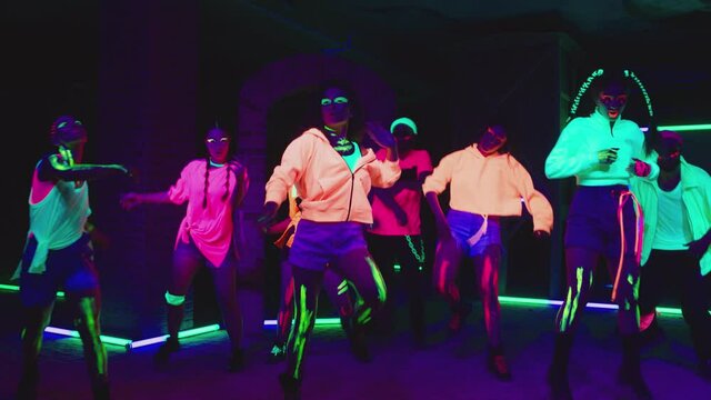 Group of female and male stylish dancers dancing inside dark place with neon lights .  Beautiful young people with fluorescent colorful make-up and clothes dancing in UV light. HD video in slow motion