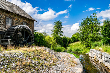 Beautiful summer rustic countryside landscape with a water mill and an old stone house. Tourist attractions and nature in Limburg. Artistic landscape with a farmhouse and a river against the blue sky.