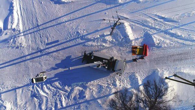 Hydraulic lift truck with moving empty cradle near poles with power transmission lines in snowy field at sunset upper view