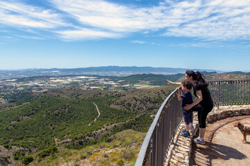 Mom with her young son on the railing of a lookout point, showing him the landscape in the distance with her finger.