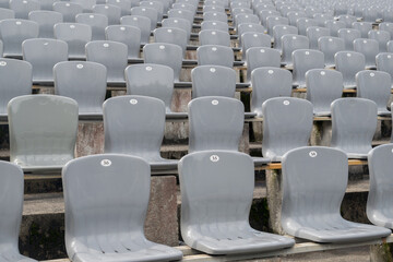 Rows of gray plastic chairs with numbers on the backs, installed in rows on cement tables in the street area, a selective focus. The front view of the seats, going into a blurry perspective.