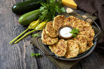 Healthy summer food, zucchini fritters. Vegetarian zucchini pancakes with cheese, served with sour cream on a rustic wooden table. Copy space.