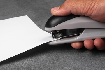 A man's hand staples documents with a stapler.
