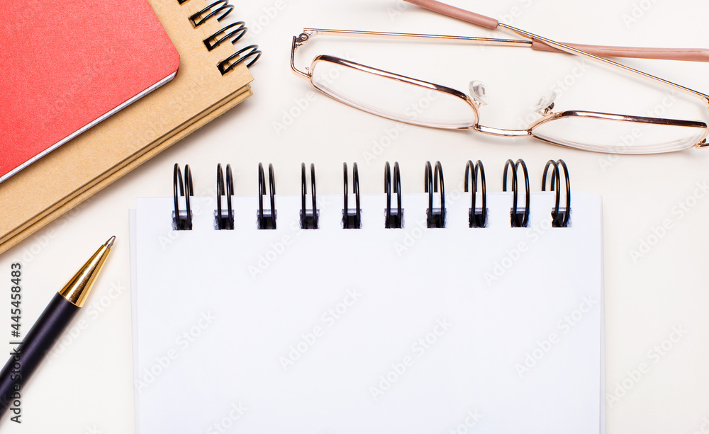 Aufkleber on a light background - glasses in gold frames, craft and red notebooks and a white blank notebook w
