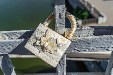 Closed love padlock with flower and pearl decoration hanging on bridge above river