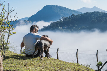 A man and a Pit Bull dog admiring nature and the great fog in the mountains of Petrópolis, Brazil,...
