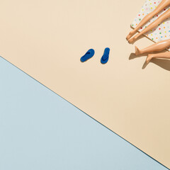 Summer scene with sunbathing towel and flip flops. Doll legs creative concept flat lay.