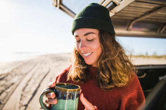 Young woman enjoying cup of coffee in the morning beach car camping