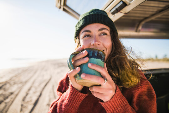 Young woman enjoying cup of coffee in the morning beach car camping