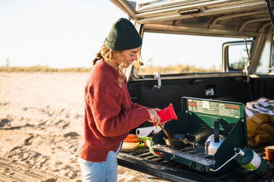 Young woman tailgate cooking while beach car camping alone