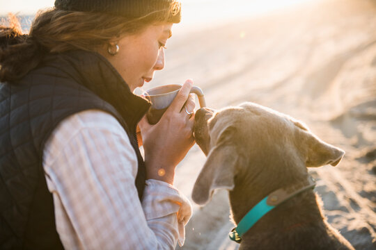 Young woman enjoying drink in mug while beach car camping with dog