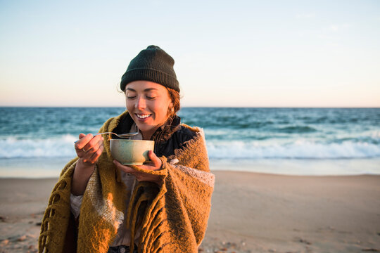 Young woman enjoying bowl of soup while beach car camping in fall