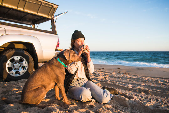 Young woman enjoying drink in mug while beach car camping with dog