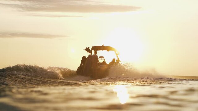 Wakeboat going in to the lake in early morning during sunrise. Slow motion shot of speed boat silhouette in horizon.