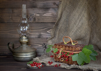 Still life of ripe red currant berries on a wooden table with a kerosene lamp in the background.