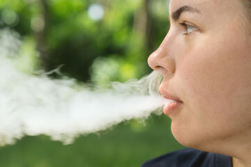 VAPE Smokes. The girl lets out smoke from her mouth and nose in close-up. Portrait of a smoking...
