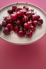 Closeup view of a white ceramic dish full of bright appetizing cherries on a pink background.
