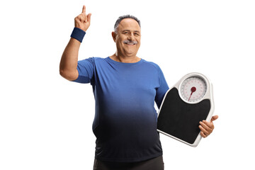 Cheerful mature man in sportswear holding a weight scale and pointing up