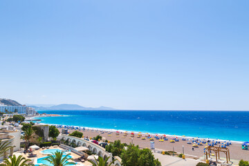 Naklejka premium Colorful umbrellas and sunbeds on an empty beach resort - vacation concept on Greece islands in Aegean and Mediterranean seas. Elli Beach in Rhodes city.