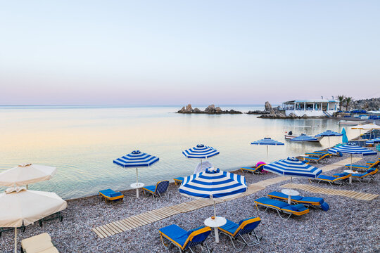 Umbrellas and sunbeds on an empty evening beach resort - vacation concept on Greece islands in Aegean and Mediterranean seas. Beach in a closed bay in a small village Charaki on a east coast of Rhodes