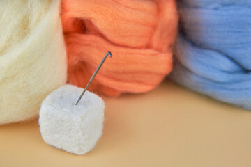 Needle in a felted cube and skeins of wool for felting.